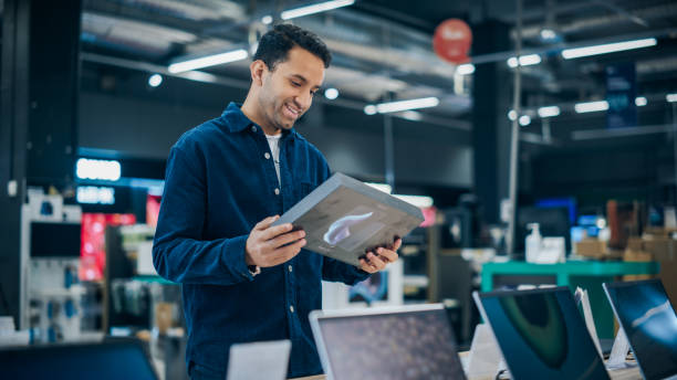 istock Handsome Young Man Shopping for a Tablet in a Home Electronics Store. Multiethnic Customer Comparing Computer Features, Sale Prices and Screen Quality in Department Showroom 2065392253
