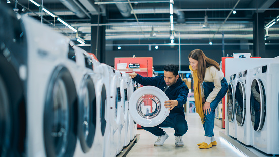 Multicultural Couple Evaluates Washing Machine Choices at Home Electronics Store. Man and Woman in Search of a Reliable Laundry Appliance. Customers Explore Modern Laundry Solutions in Retail Shop