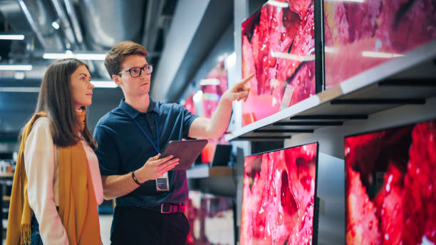 portrait of a female customer seeking advice from retail home electronics expert. young lady explores modern tv options. shopper evaluating latest television innovations in elegant department store - department store clothing showroom people photos et images de collection