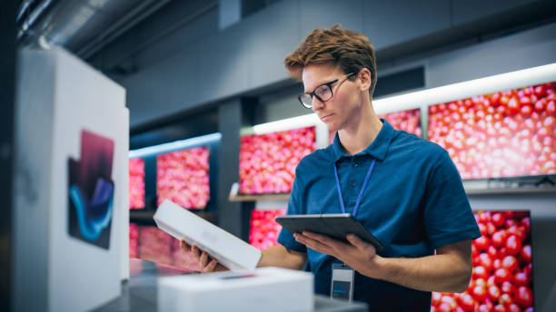 istock Portrait of a Sales Representative in Home Electronics Store Using Tablet Computer for Online Workflow. Young Staff Member Manages Inventory, Product Availability and Customer Orders from Internet 2065398520
