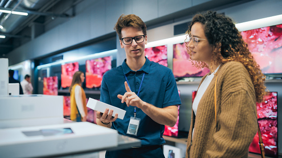 Portrait of Female Customer Seeking Advice from Retail Home Electronics Expert. Hispanic Girl Explores Smartphone Options. Shopper Evaluating Latest Mobile Phone Innovations in the Department Store