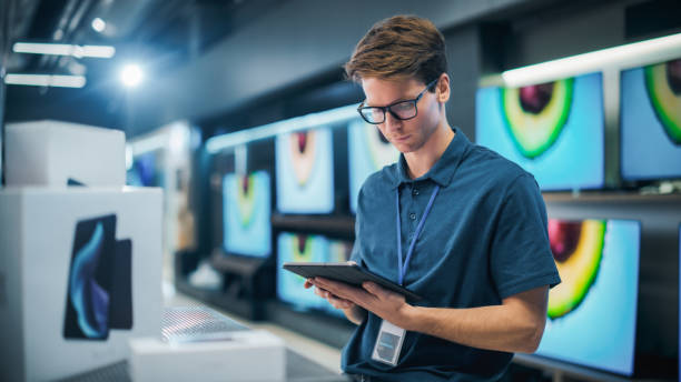 istock Portrait of Sales Representative in Home Electronics Store Using Tablet Computer for Online Workflow. Young Staff Member Manages Inventory, Product Availability, and Customer Orders from Internet 2065401721