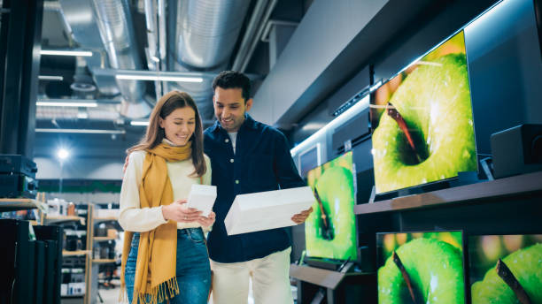 stylish multiethnic couple is shopping at retail electronics store. man and female found great deals on a modern smartphone and tablet computer combo. customers walking and discussing tech features - department store clothing showroom people ストックフォトと画像