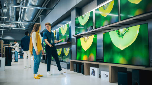 istock Young Female Shopper Having Conversation with Electronics Store Sales Rep. Stylish Lady Explores Sleek Flat-Screen TV Options. Customer Seeking Impressive Television Solutions in Modern Retail Store 2065405926