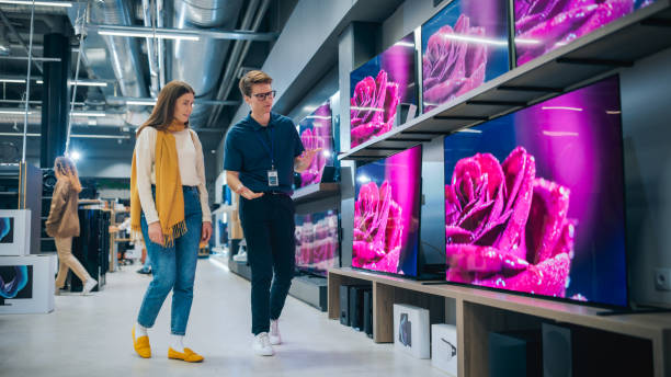 istock Young Female Shopper Having Conversation with Electronics Store Sales Rep. Stylish Lady Explores Sleek Flat-Screen TV Options. Customer Seeking Impressive Television Solutions in Retail Store. 2065406459