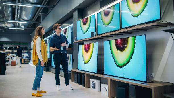 istock Young Female Talking with Retail Electronics Store Associate. Stylish Woman Seeks High-Quality Flat-Screen TV. Shopper Exploring Latest Television Options in Contemporary Retail Storefront 2065406501