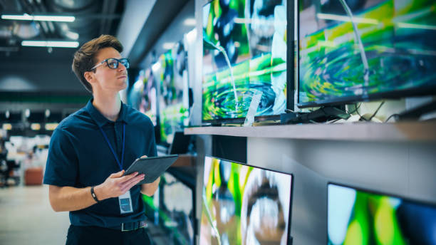 Young Sales Manager in Home Electronics Store Expertly Manages Operations Using Tablet Computer. Professional Oversees TV Sets Inventory and Product Updates with Technological Efficiency