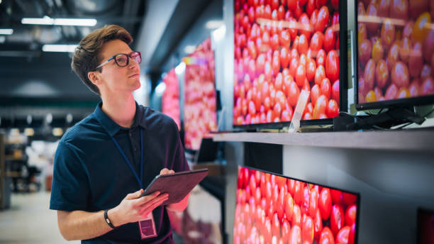 istock Young Sales Manager in Home Electronics Store Expertly Manages Operations Using Tablet. Professional Oversees TV Sets Inventory and Product Updates with Technological Efficiency. 2065410883