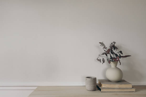 istock Modern vase with dry eucalyptus tree branches on wooden table. Candle in concrete candleholder, pile of old books. White wall background. Scandinavian interior. Elegant home decor. Empty copy space. 2065451238