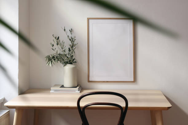 istock Empty vertical picture frame mockup. Wooden desk, table. Vase with olive branches, magazines. Elegant working space, home office. Summer interior design. Beige walls. Blurred palm leaf overlay. 2065452304