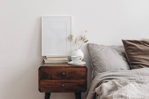 istock Vertical white picture frame mockup on old books. Elegant bedroom view. Brown, grey linen and velvet pillows, blanket. Wooden night stand with ceramic vase, dry grass and cup of coffee. Scandinavian interior. 2065453371