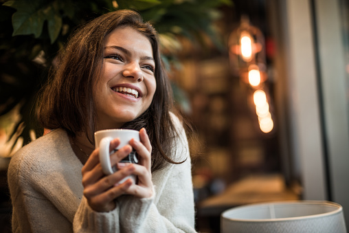 Nice student drinks coffee in the cafeteria and enjoys the atmosphere with a smile