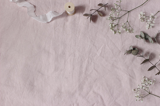 Floral wedding, birthday table composition. Gypsophila, eucalyptus tree leaves leaves and silk ribbons on pink linen table cloth background. Flat lay, top view. Copy space. No people.
