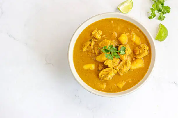 Thai Chicken Curry in a Bowl with Cilantro and Lemon on White Background