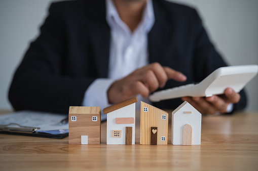Professional Evaluating Wooden House Models. Businessperson with calculator analyzing wooden house models, concept of real estate evaluation. Finance home loan or interest concept.