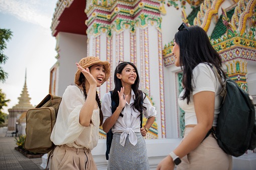 Women tourists with backpacks standing by the temple in Bangkok.