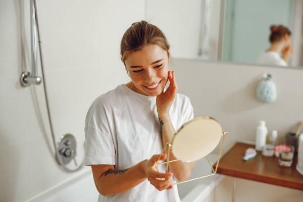 istock Young beautiful lady looking at her face in a small round mirror doing routine skincare procedures 2065481545