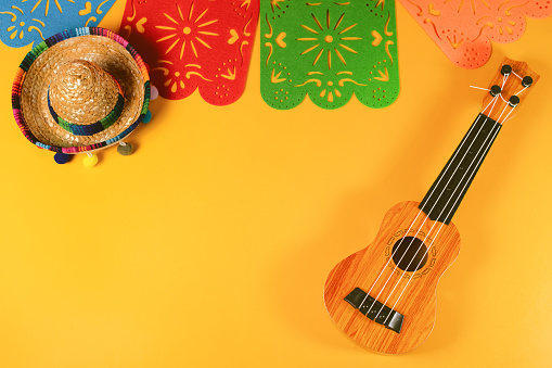 Traditional paper flag, guitar and large sombrero for Cinco de Mayo holiday party celebration on yellow table.