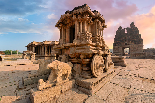 Famous ancient stone chariot of Hampi in closeup view with other architecture ruins at Karnataka, India, at sunset.