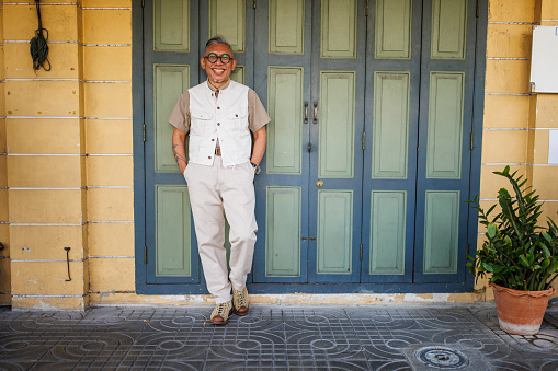 Mature Asian man standing by the wooden door outdoors.