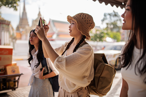 Women tourists with backpacks walking on sidewalk in Bangkok.