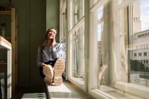 Businesswoman sitting on window sill using smart phone