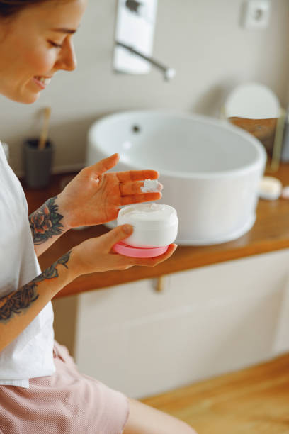 istock Smiling young woman use jar with face cream while standing in bathroom. Home beauty routine 2065495868