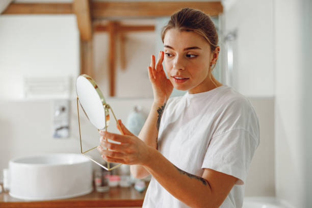istock Young woman looking in small round mirror and checking skin while standing in bathroom 2065499626