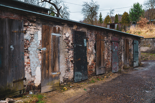 An image of an old, run-down building with broken doors and windows, showing signs of decay and neglect. The weathered facade and overgrown surroundings highlight the buildings abandonment and deterioration.