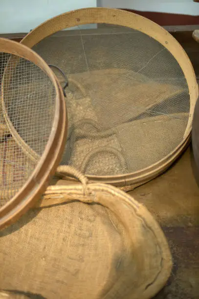 Wooden and metal mesh sieves resting on a sackcloth surface and a handmade minbre basket, evoking a rustic and traditional atmosphere.
