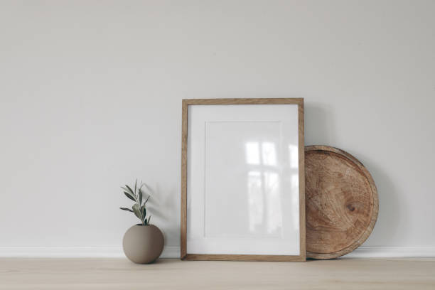 istock Blank vertical picture frame mockup, poster display. Ball vase with olive tree branch. Round wooden tray on table, desk. Minimal rustic home. Scandinavian interior. White wall background. 2065521632