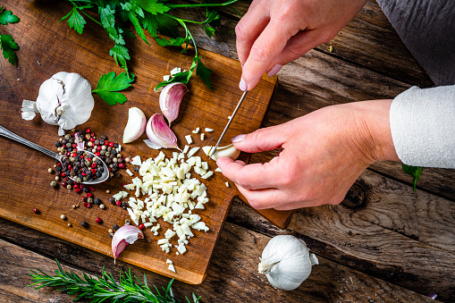 Overhead view of hands chopping garlic on wooden cutting board