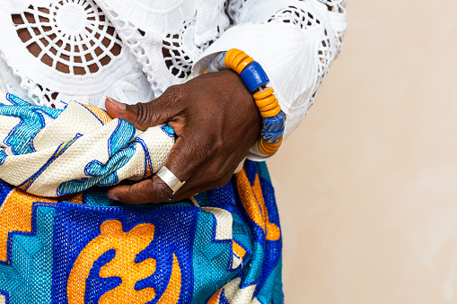 A detailed close-up highlights the hands of an African person clad in vibrant traditional attire, adorned with colorful beads and a woven bracelet, exemplifying the intricate beauty of African cultural garments