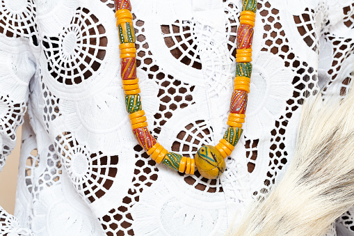 A detailed close-up shot highlighting the intricate design of a traditional African necklace laid on an embroidered white garment, emphasizing the colorful patterns and craftsmanship