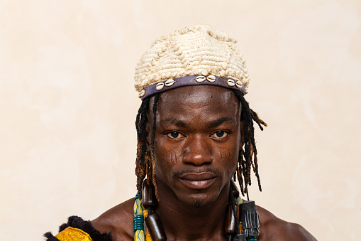 Close-up portrait of an African man showcasing traditional adornments, featuring a cowrie shell headband and a vibrant beaded necklace, reflecting his cultural heritage