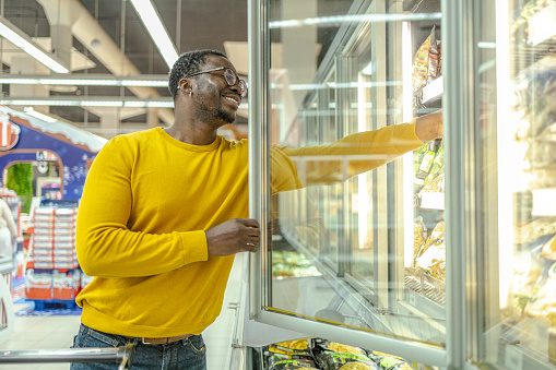 Photo of african-american ethnicity man choosing groceries from fridge in supermarket
