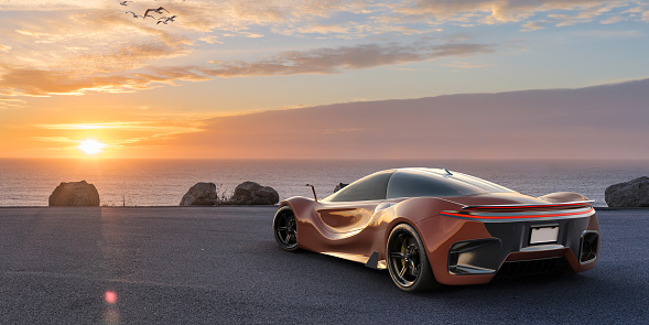 Close up rear view of a modern generic red electric sports car parked next to the coast with a view out to sea at dawn. With copy space.