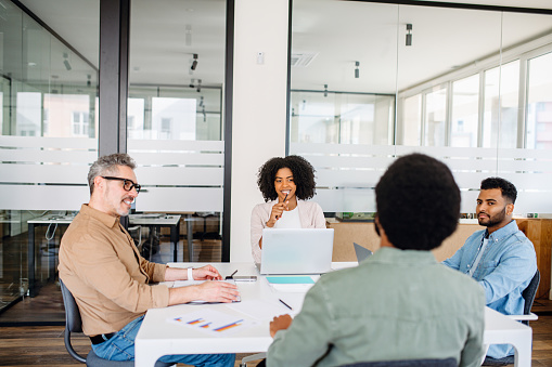 A diverse group of professionals collaborates in a modern office space, with a woman in a white blazer leading the discussion, indicative of a team brainstorming session.