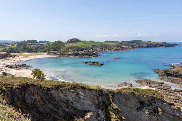 istock a serene beach with turquoise waters, surrounded by rocky terrain and lush greenery under a clear sky. A few people are visible in the distance 2065629162