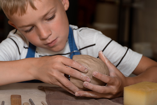 School boy sculpting mug from wet clay in hobby class