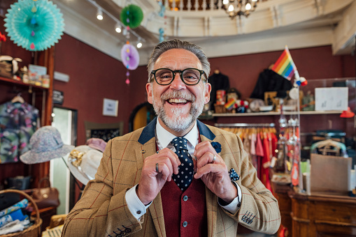A mature man enjoying a day out shopping in a vintage clothing store in Durham, North East England. He is standing in the shop, looking at the camera and smiling as he shows off his tie.
