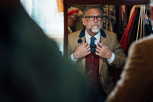 A mature man enjoying a day out shopping in a vintage clothing store in Durham, North East England. He is looking in the mirror to check out how his outfit looks while adjusting his clothing.