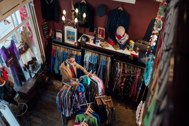 A mature man enjoying a day out shopping in a vintage clothing store in Durham, North East England. He is standing in the shop, looking through the clothing rails at the merchandise for sale.