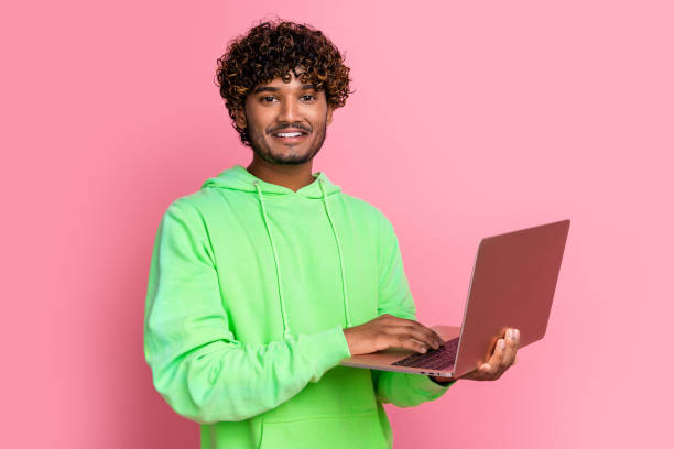 istock Photo of cheerful young man indian guy curly hair student studying using netbook online while pandemic isolated on pink color background 2065660382