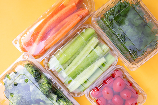 Vegetables in plastic containers on yellow background