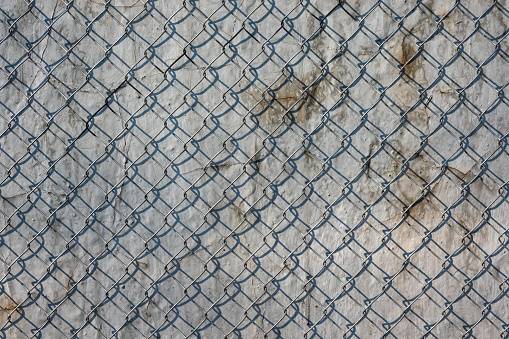 Steel mesh netting on the background of a gray metal wall. Smudges, cracks and shadows from the mesh on the surface are visible. Background. Texture.