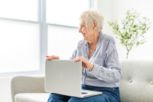 пожилые женщины используют ноутбук, сидя в офисе - one person lifestyles 80 plus years indoors стоковые фото и изображения