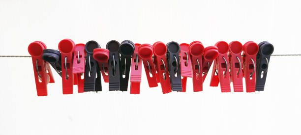 A close up, shot of purple clothes pegs standing in a line on a white background. The focus is on one of the pegs in the middle of the row which is lying down.