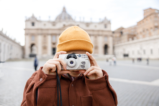 A Girl wearing a yellow hat is taking a picture with a old film camera and the hat is covering their face