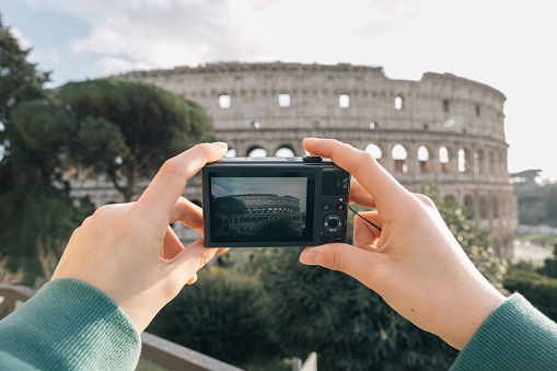 A girl takes pictures of the Roman Colosseum with her small digital camera